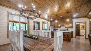 A wooden-paneled kitchen with a central island, white chairs, and a chandelier.