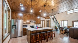 A spacious kitchen with wooden cabinets, a stainless steel refrigerator, and a large island with bar stools.