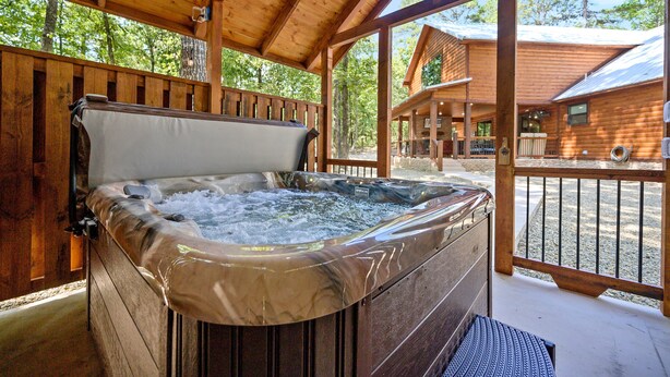 A hot tub in a wooden cabin with a deck and a view of another cabin.