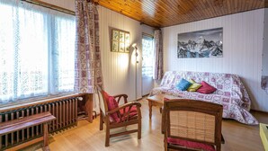 A cozy room with a wooden ceiling, a sofa with patterned cushions, a wooden chair, and a radiator.