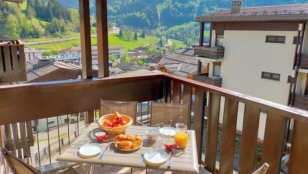 A balcony with a table set for breakfast, overlooking a mountainous landscape.