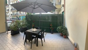 Un pequeño patio al aire libre con una mesa, sillas, un paraguas grande y plantas en macetas.