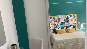 Un dormitorio moderno con una cama, una silla, un espejo y una mesita de noche.