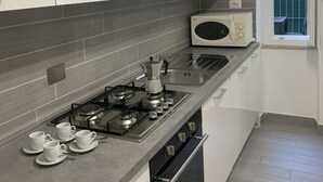 Una cocina moderna con armarios blancos, estufa a gas, microondas y ventana con persianas.