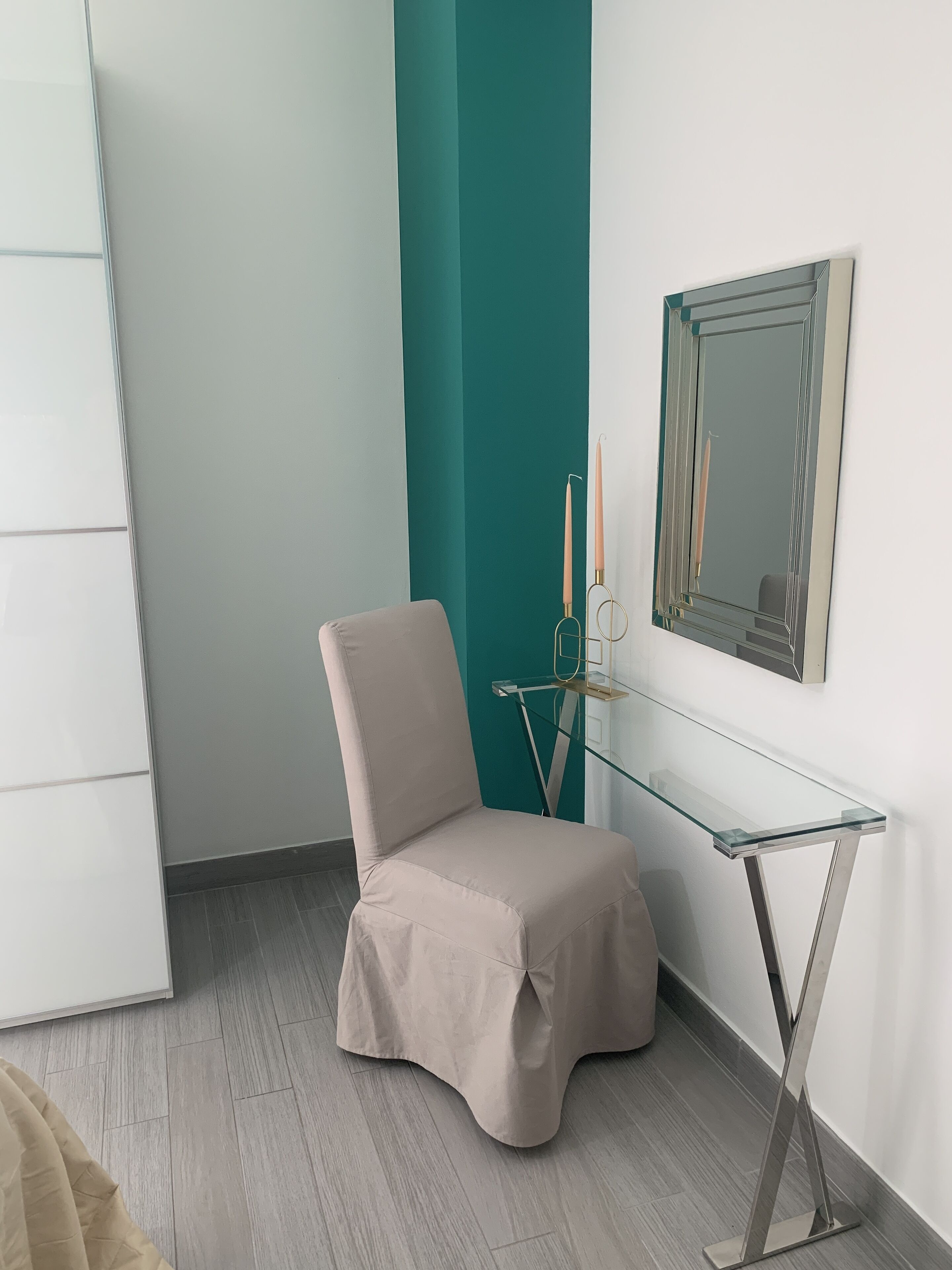 Une pièce d’angle avec un fauteuil beige, une table en verre, un mur d’accent de couleur turquoise et un miroir.