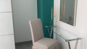 Habitación de esquina con una silla color crema, una mesa de vidrio, pared de acento color turquesa y un espejo.