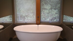 A modern bathroom with a freestanding bathtub, wooden window frames, and a view of trees outside.