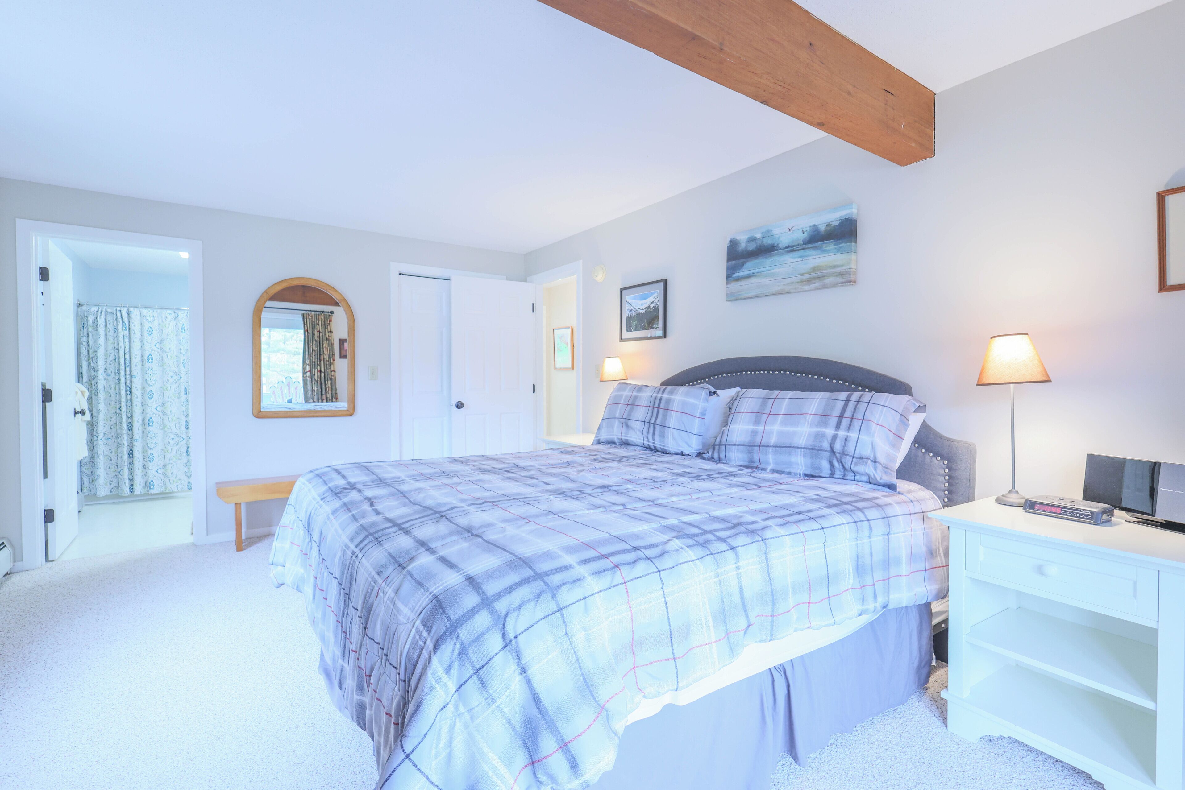 A bedroom with a bed, bedside table, lamp, and a painting on the wall.