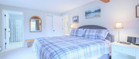 A bedroom with a bed, bedside table, lamp, and a painting on the wall.