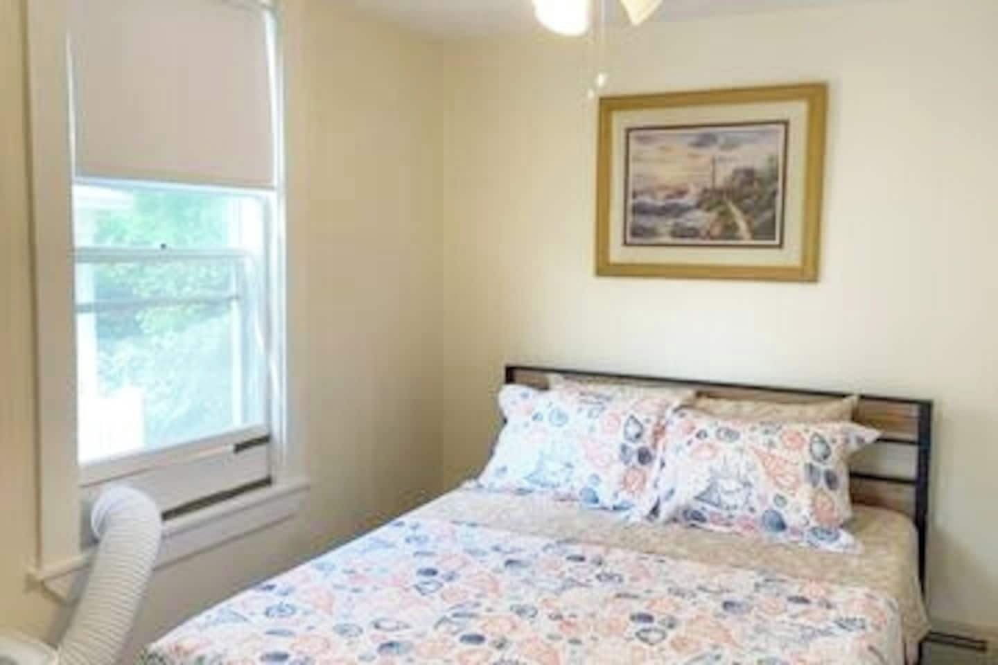 A bedroom with a bed, a window, and a framed picture on the wall.