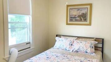 A bedroom with a bed, a window, and a framed picture on the wall.