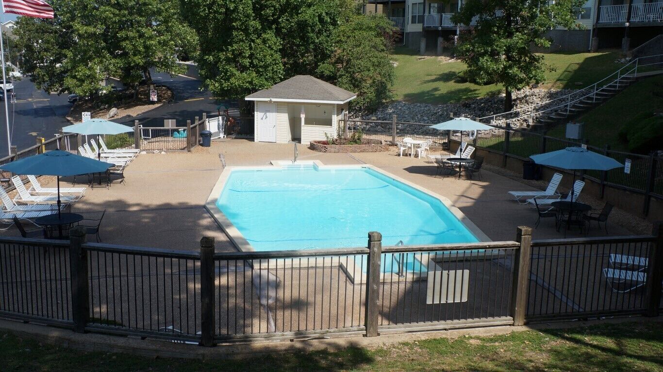 A swimming pool with lounge chairs and umbrellas, surrounded by a wooden fence.