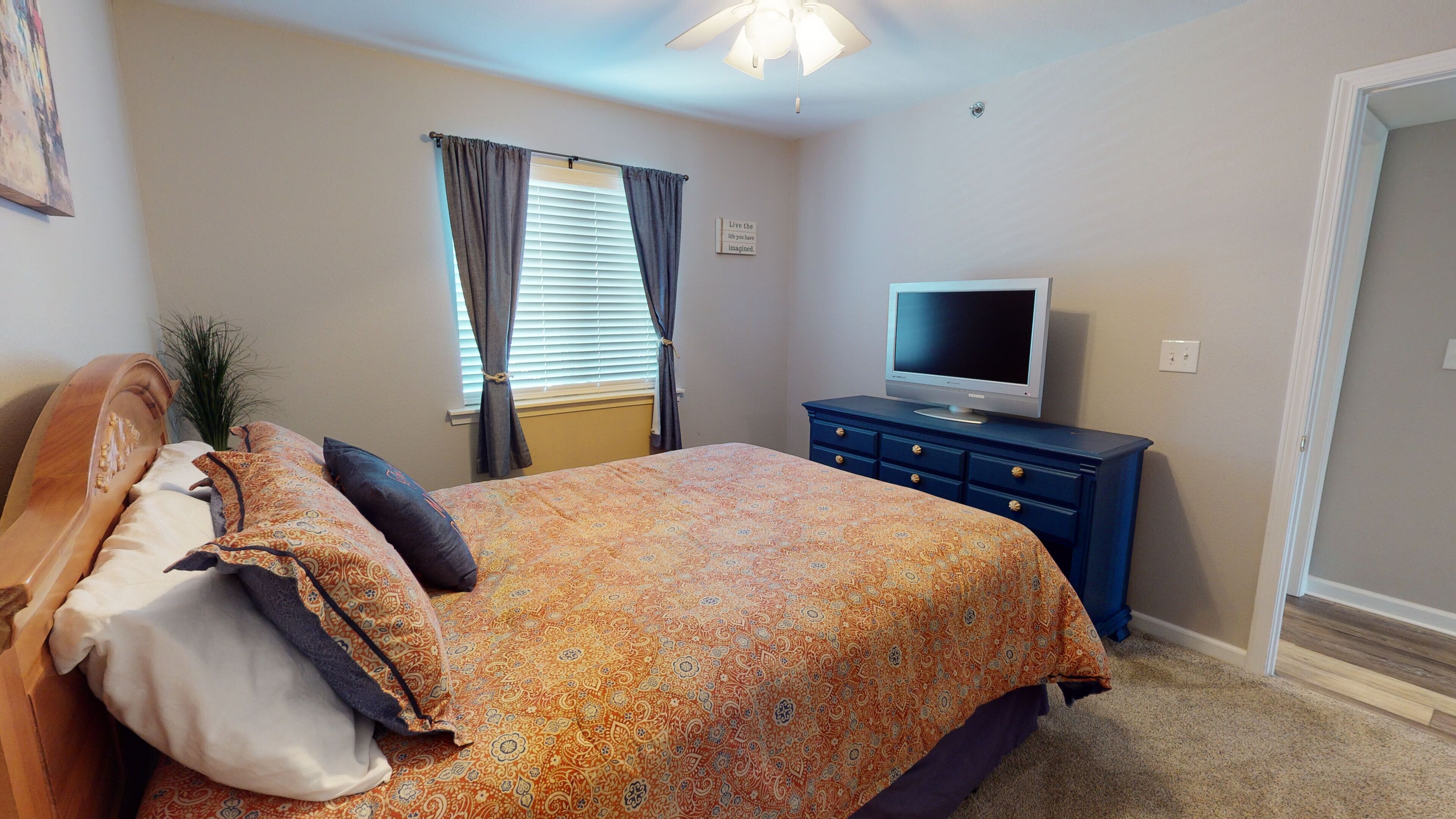 A bedroom with a bed, a television on a dresser, and a window with curtains.
