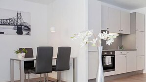 A modern kitchen with white cabinets, a dining area with two chairs and a table, and a vase with flowers. - Spreepolis Boardinghouse (Berlin-Oberschöneweide)