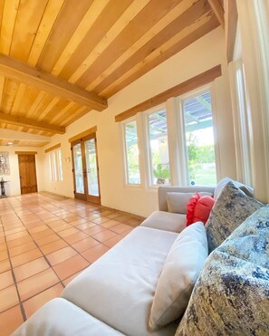 A spacious room with a high wooden ceiling, a tiled floor, and a large window providing a view of the outdoors.