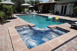 A swimming pool with a hot tub and lounge chairs.