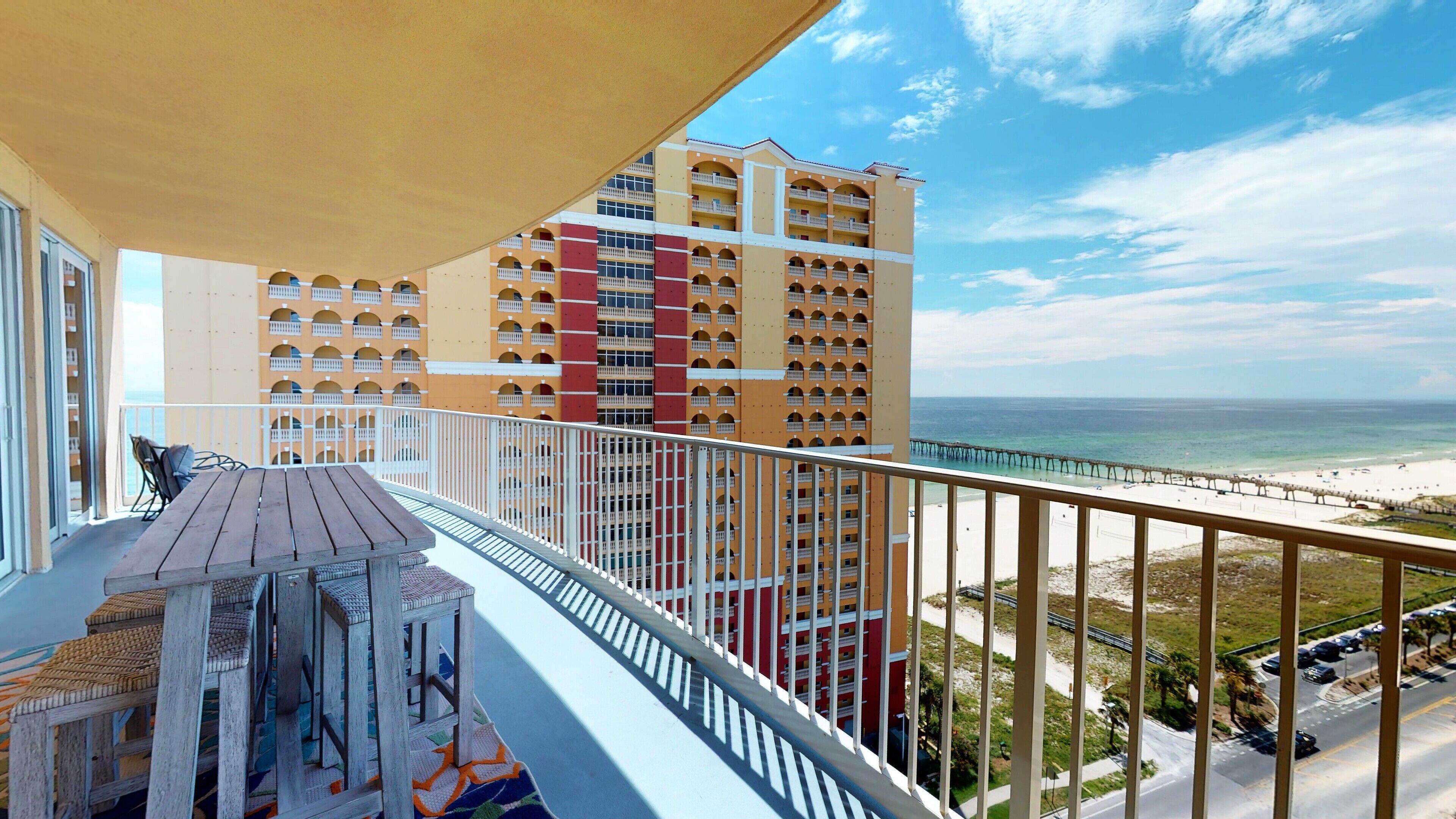 A balcony with a view of a beach and a pier, overlooking a multi-story building with balconies.