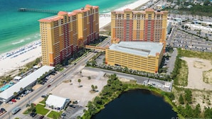 A high-rise hotel with multiple floors, a parking lot, and a beach view.