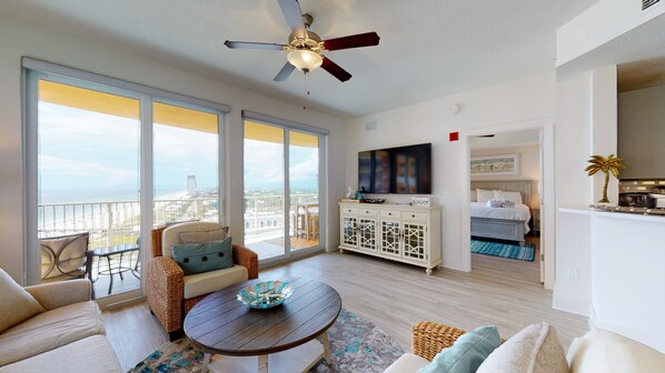 A spacious living room with a balcony, a ceiling fan, a TV, and a dining area.