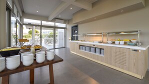 Un moderno montaje de bufé con varias estaciones de servicio, un amplio ventanal que proporciona luz natural y una decoración interior limpia y contemporánea.