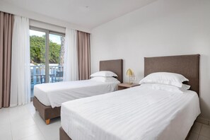 A hotel room with two beds, a balcony with curtains, and a view of greenery outside. - Smaragdi Kos Hotel (Kos)