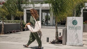Una persona caminando al lado del cartel de Kos Hotel, con un edificio moderno de fondo.