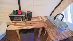 Une cuisine compacte équipée d’un four à micro-ondes, d’une machine à café et d’une casserole en métal posée sur une table en bois.