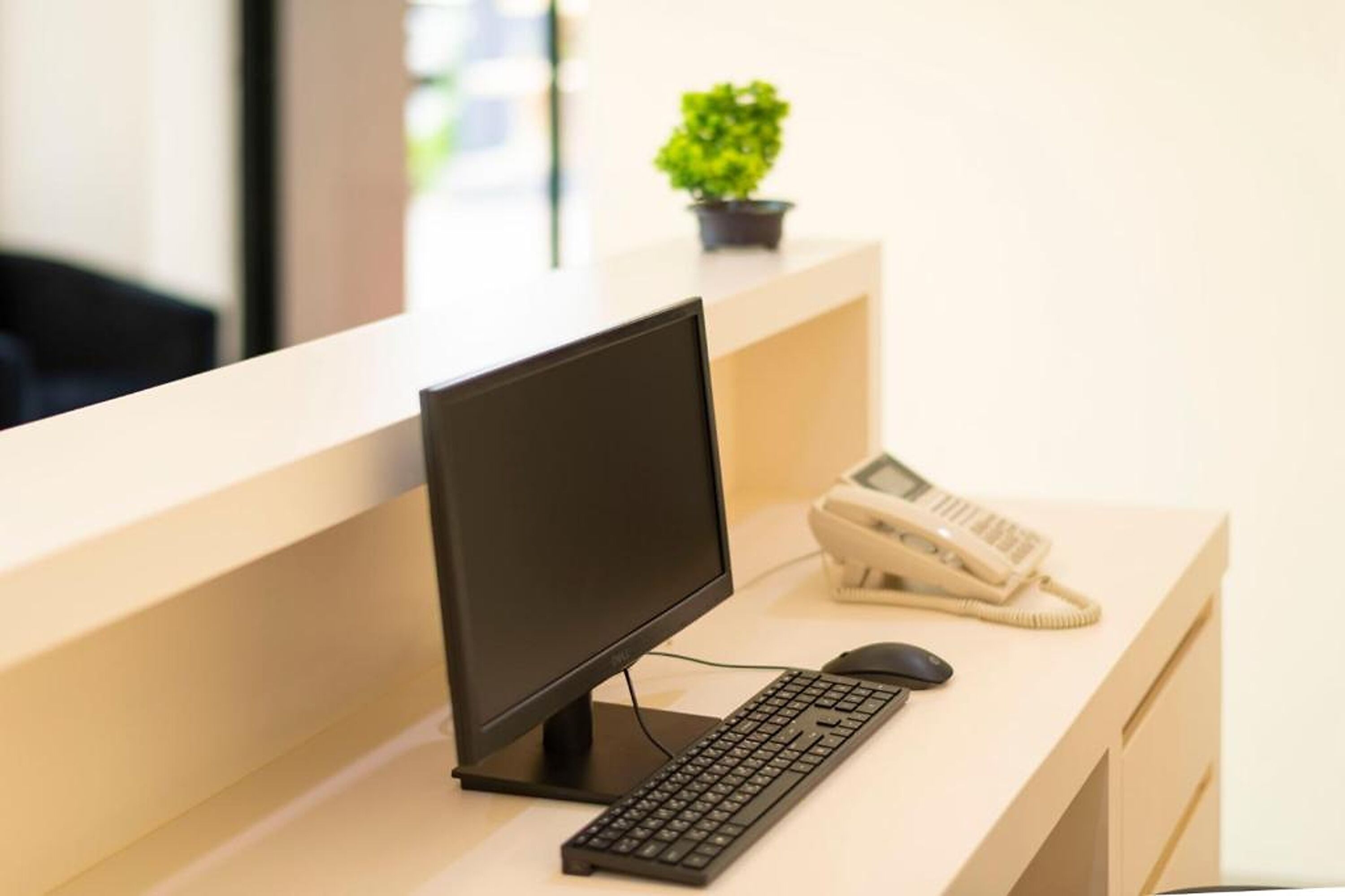 A modern office desk with a computer monitor, keyboard, and telephone.