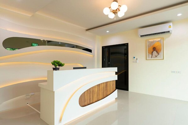 A modern reception desk with a wooden accent, a potted plant, and a wall-mounted air conditioner. - Thip Thip Hotel (Krabi)