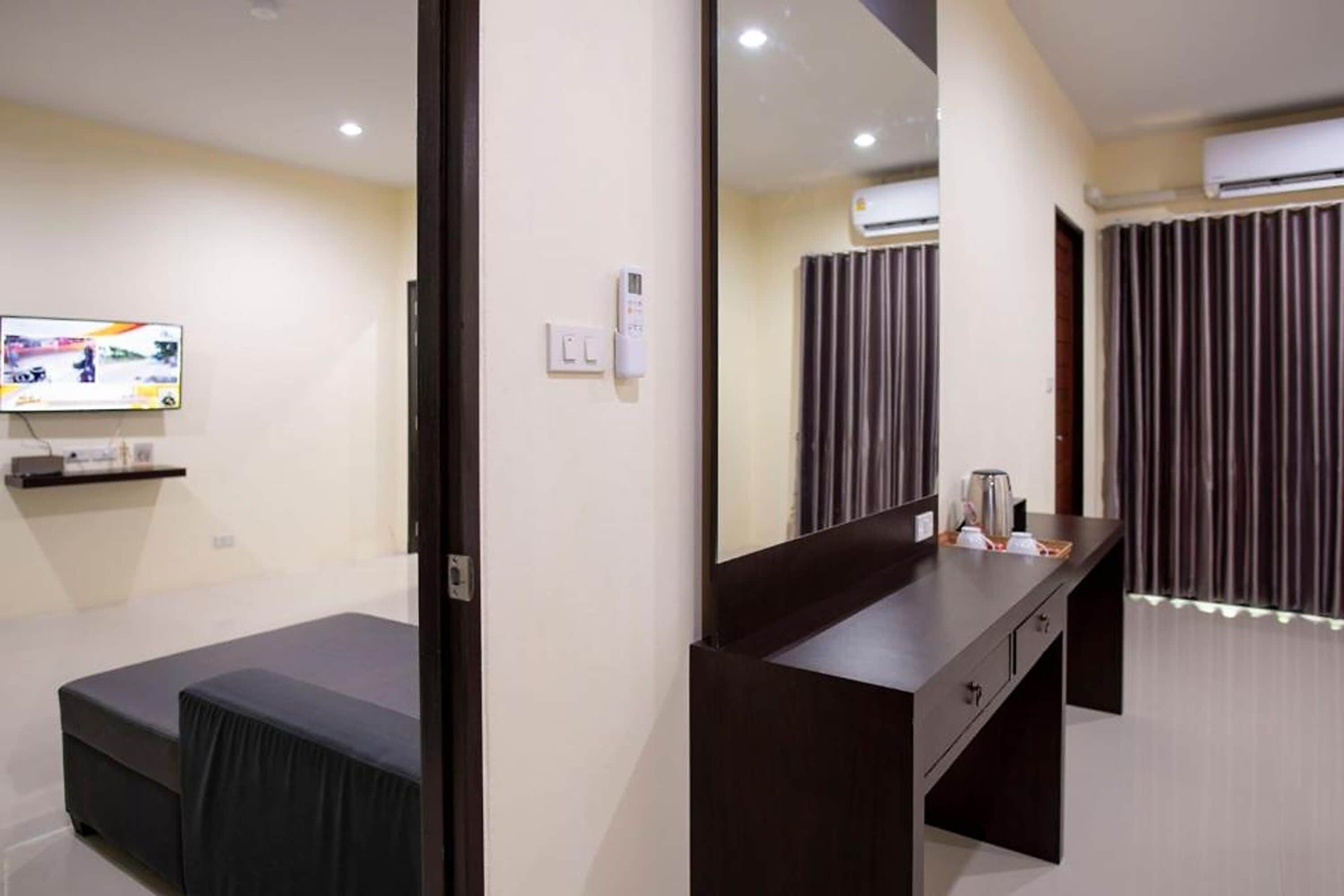 A hotel room with a bed, a desk with a mirror, a television on the wall, and an air conditioning unit.