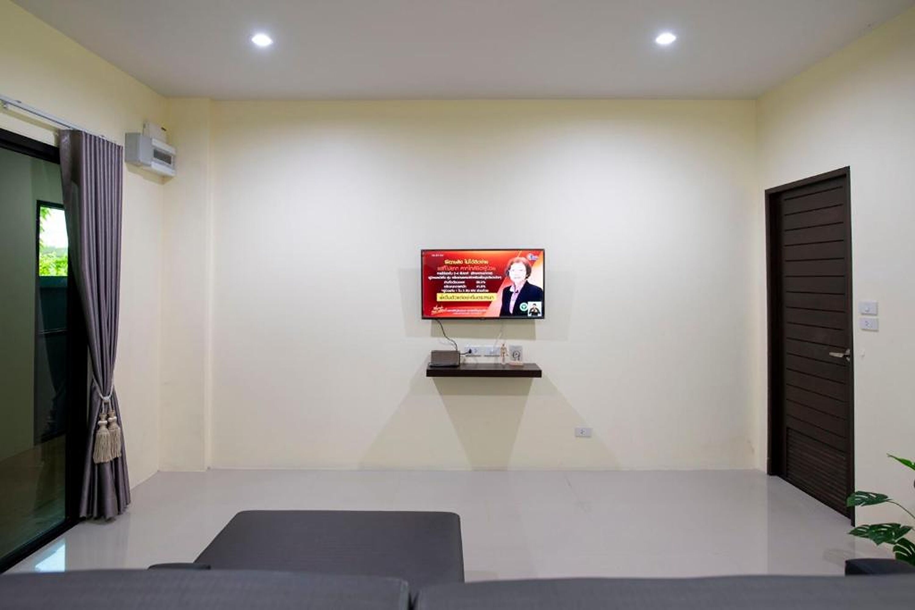 Una habitación con una televisión de pantalla plana en la pared, una puerta oscura y una ventana con cortinas.