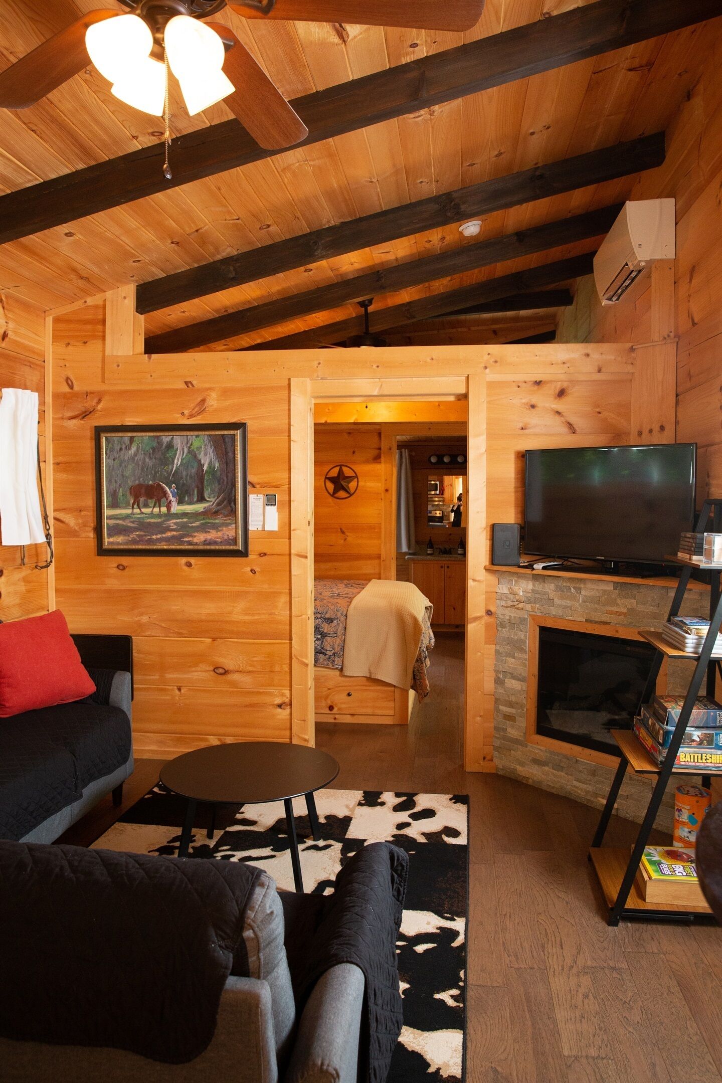 Ein gemütliches Blockhaus-Interieur mit Holzbalkendecke, Kamin, Fernseher und Essbereich.