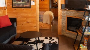 A cozy cabin interior with a wooden ceiling, a fireplace, a television, and a dining area. - Serenity Ridge Cabin E: Couple's Holiday (Mill Spring)