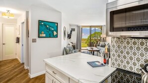 A modern kitchen with a large island, a microwave, and a view to the outside. - Modern and Relaxing Oceanfront Vistas (Kihei)