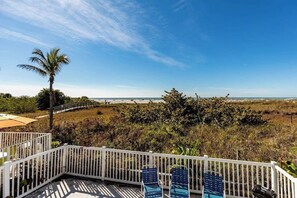 A deck with a view of the ocean, a palm tree, and a white fence.