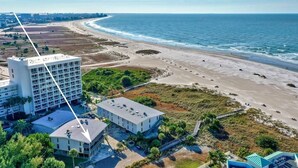 A coastal hotel with a large building, a beach, and a clear view of the ocean.