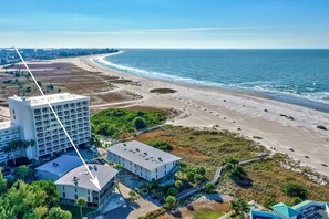A coastal hotel with a large building, a beach, and a clear view of the ocean.