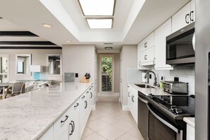 A modern kitchen with white cabinetry, a central island, a built-in oven, and a microwave.