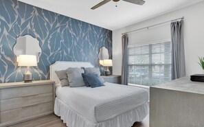 Un dormitorio con cama, dos lámparas de noche, una mesita de noche, cómoda y una ventana con cortinas.