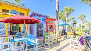 A colorful outdoor seating area with wooden tables and chairs, surrounded by various shops and a wooden deck. - 6 Seat Golf Cart ~ Sleeps 9 ~ Arcade Games (Santa Rosa Beach)