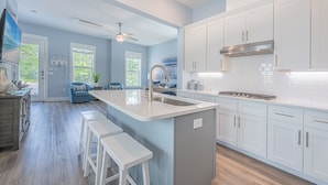 A modern kitchen with white cabinets, a central island with stools, and a large window. - 6 Seat Golf Cart ~ Sleeps 9 ~ Arcade Games (Santa Rosa Beach)
