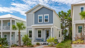 A two-story house with a front porch, a garage, and a small garden area with palm trees and shrubs. - 6 Seat Golf Cart ~ Sleeps 9 ~ Arcade Games (Santa Rosa Beach)