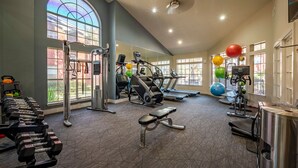 Une salle de sport équipée de divers appareils d’exercice, dotée de grandes fenêtres et d’un plafond haut.