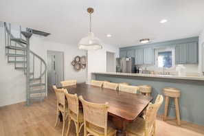 A modern kitchen with a dining area, featuring a spiral staircase, a chandelier, and light blue cabinets.