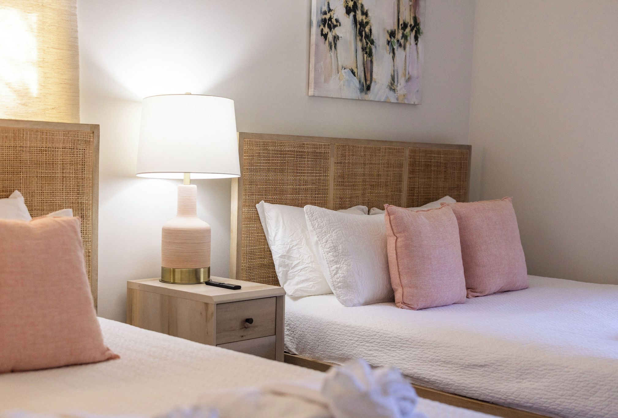 A hotel room with two beds, a bedside table with a lamp, and a painting on the wall.
