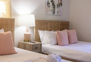 A hotel room with two beds, a bedside table with a lamp, and a painting on the wall.