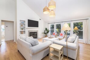 A modern living room with a fireplace, a flat-screen TV, and a large window with curtains.