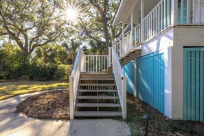A residential building with a staircase leading to a porch, surrounded by trees and a fence.