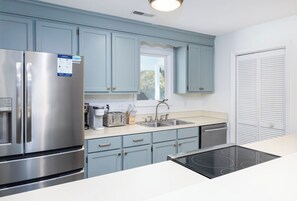 A modern kitchen with light blue cabinets, a stainless steel refrigerator, a built-in oven, and a window above the sink.