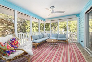 A covered porch with a ceiling fan, a wicker chair, a sofa with cushions, and a striped rug. - Tropicana Cabana with Fenced Yard (Isle Of Palms)
